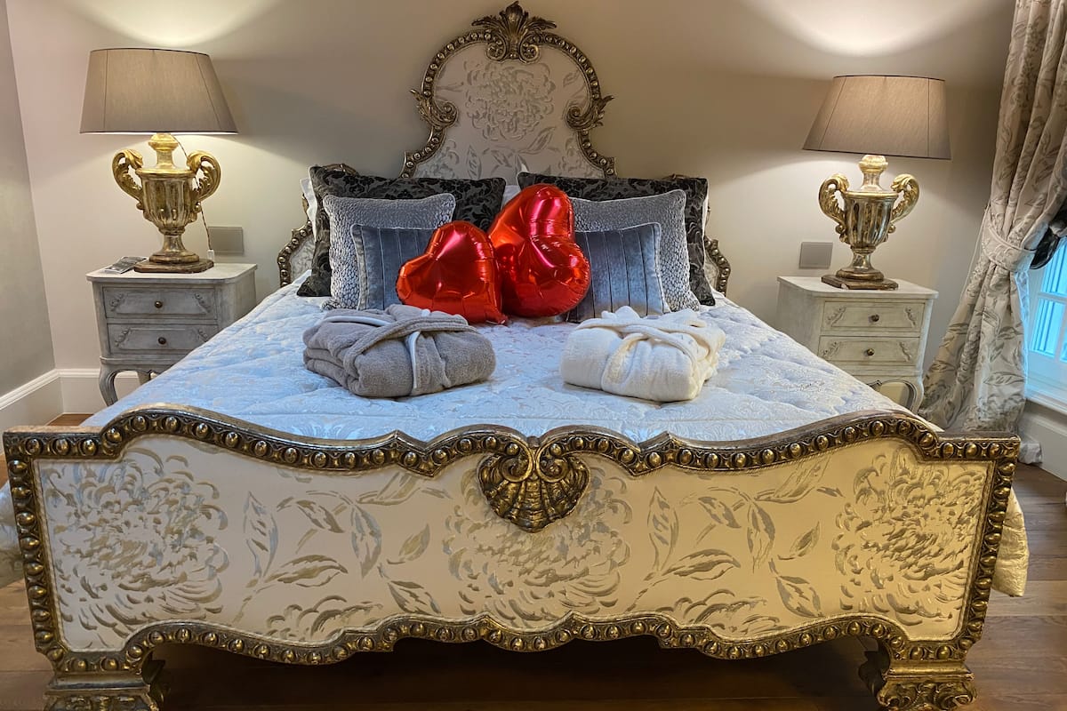 Una cama con detalles ornamentales dorados, dos lámparas de noche y un cabecero estampado con motivos florales.