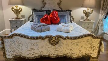 Una cama con detalles ornamentales dorados, dos lámparas de noche y un cabecero estampado con motivos florales.