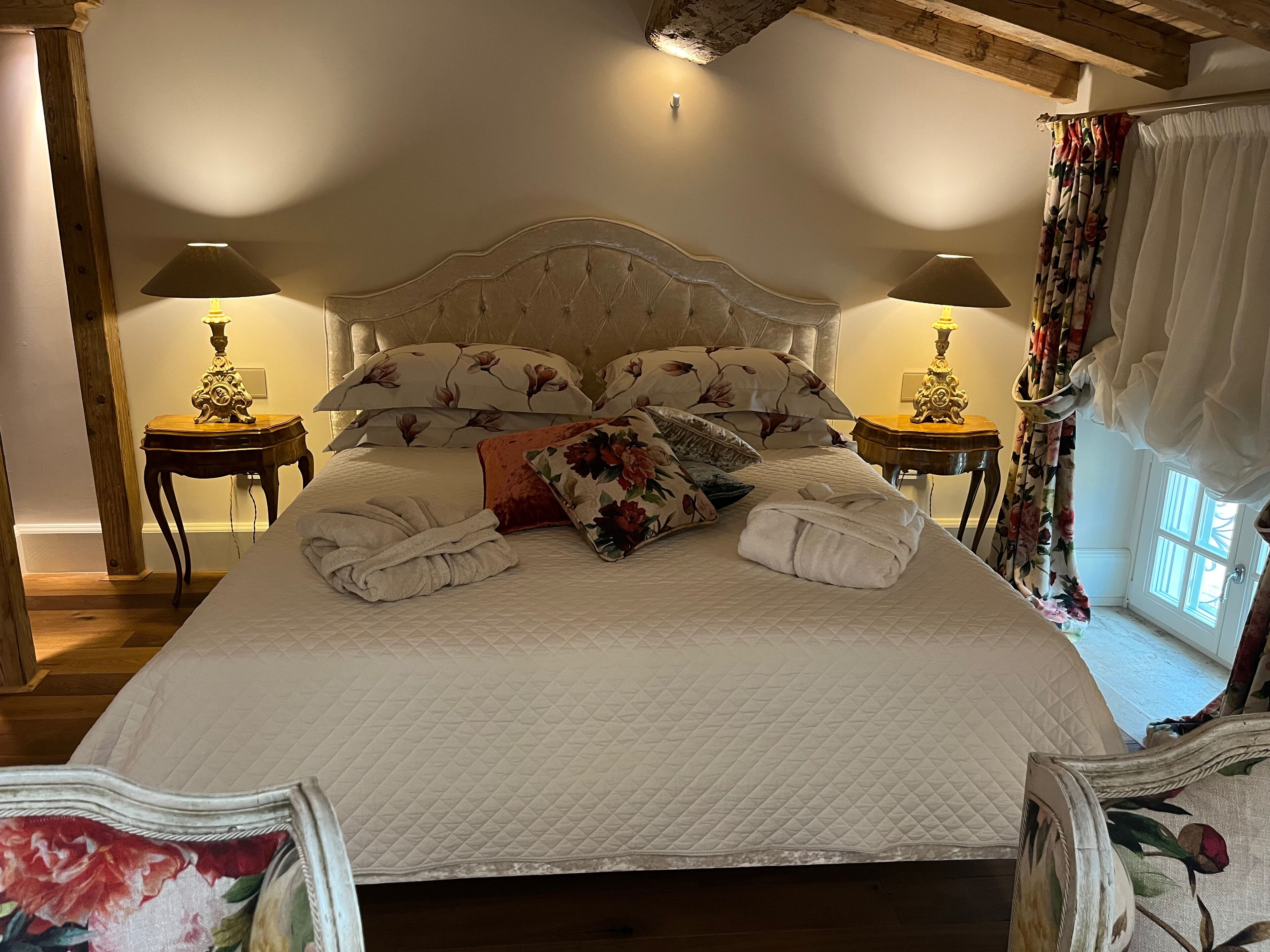 A well-appointed bedroom with a large bed, floral bedding, two bedside lamps, and a wooden headboard.