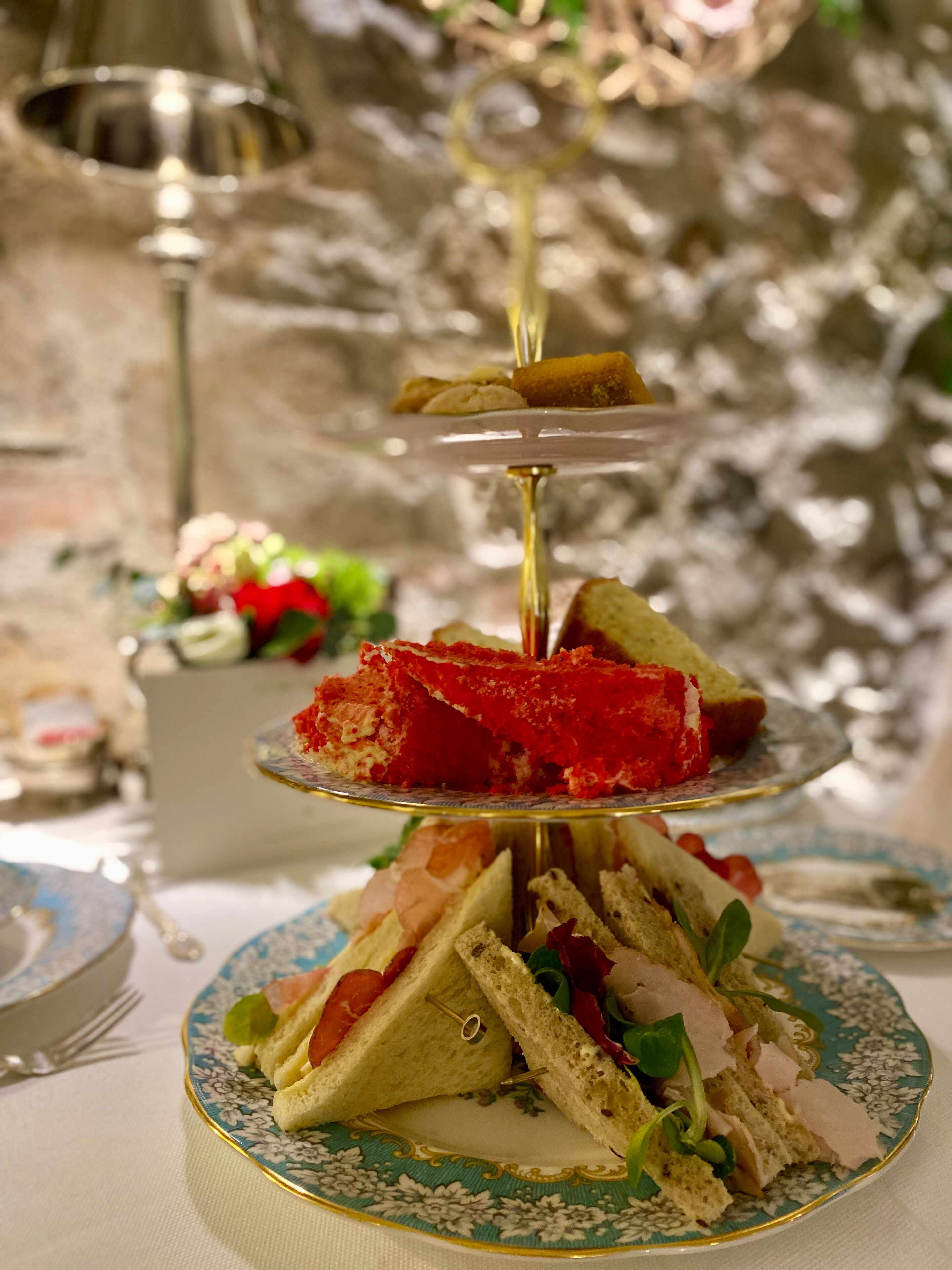 Un expositor escalonado para postres con varios pasteles y un sándwich sobre un plato floral.