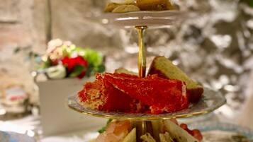 Un expositor escalonado para postres con varios pasteles y un sándwich sobre un plato floral.