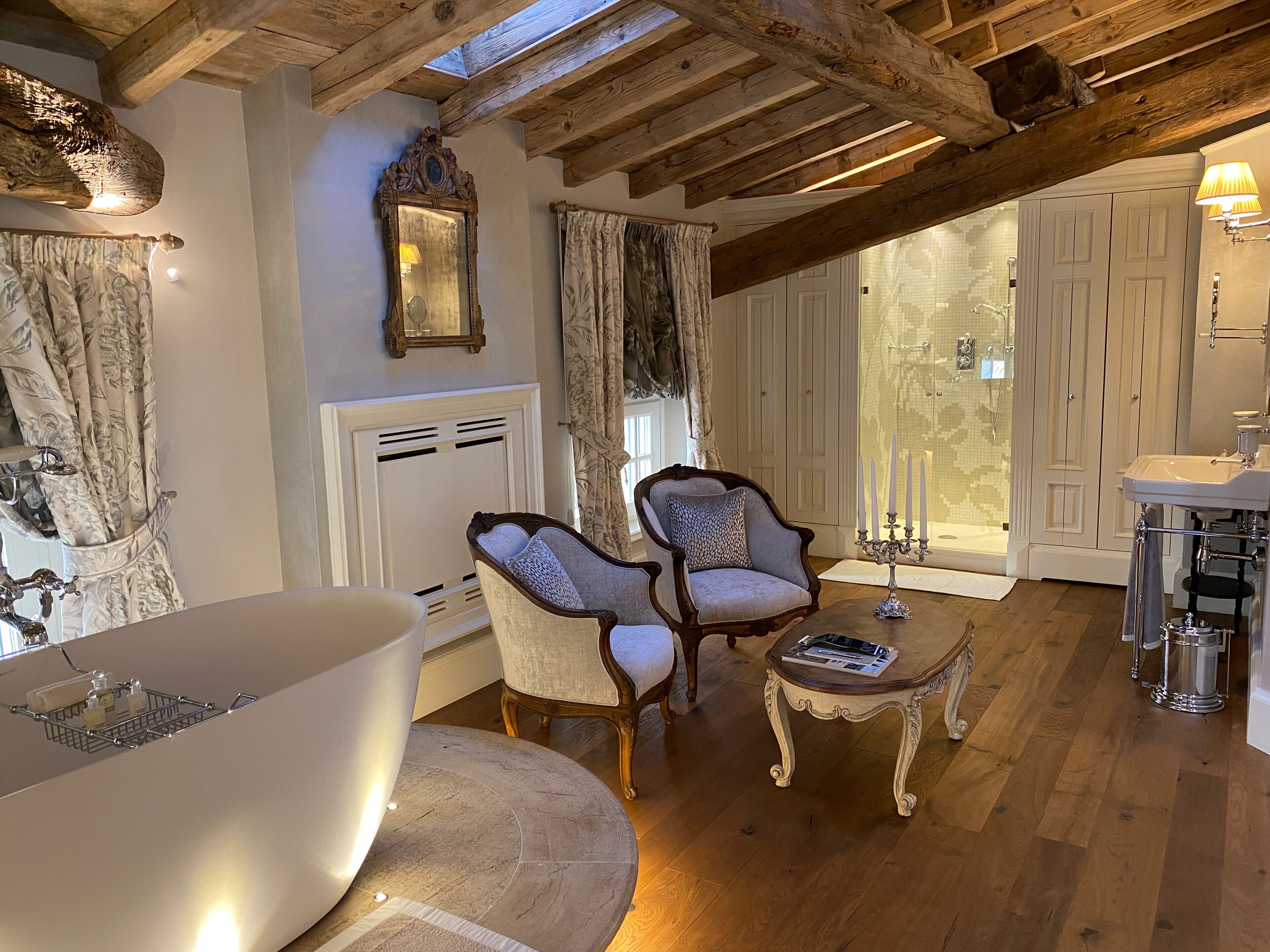 A cozy room with a large bathtub, two armchairs, a small table, and a wooden ceiling.