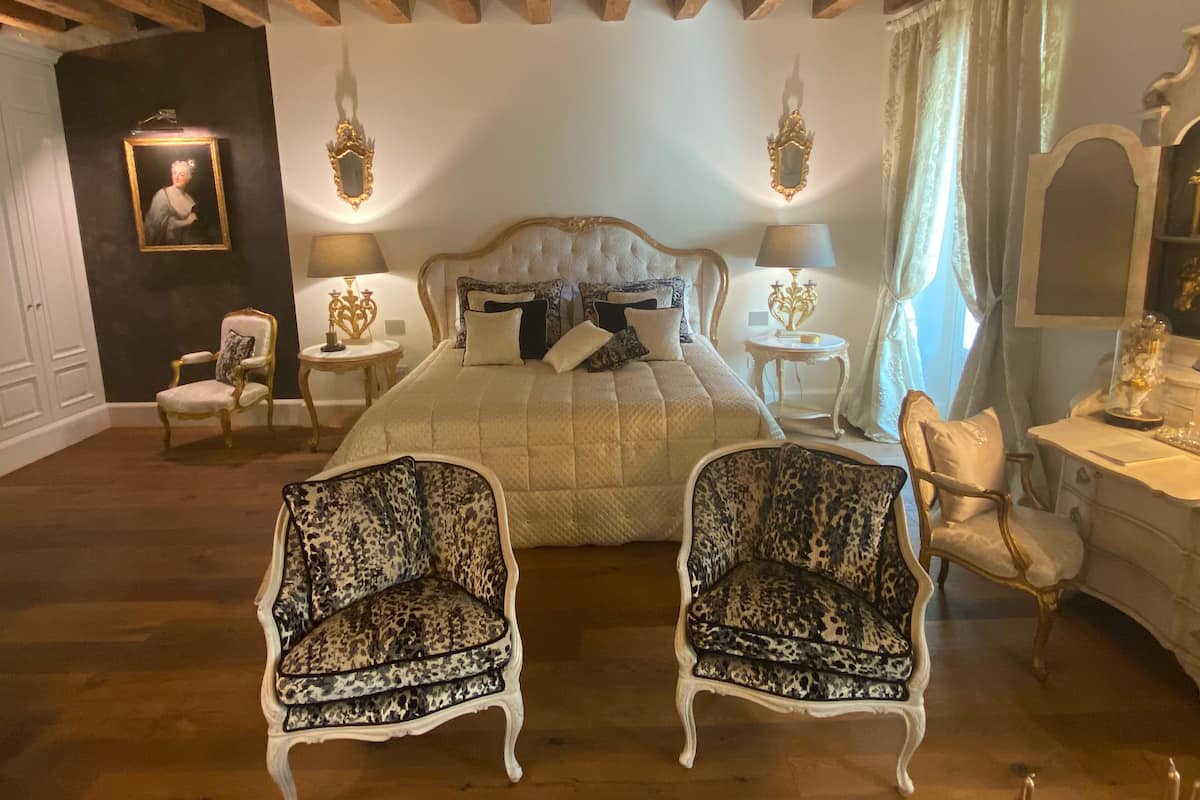 Un dormitorio con una cama grande, dos sillones, un tocador y un espejo.