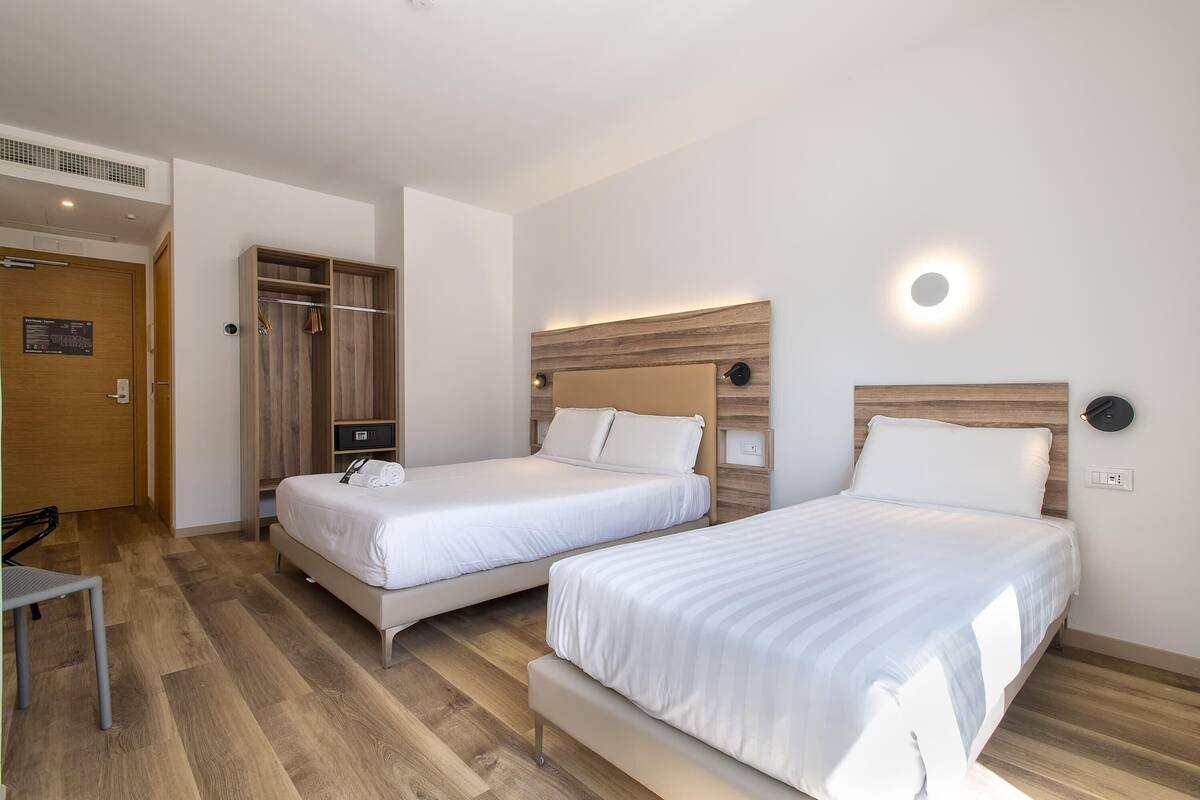 Una camera d'albergo con due letti, un armadio in legno e un tavolino.