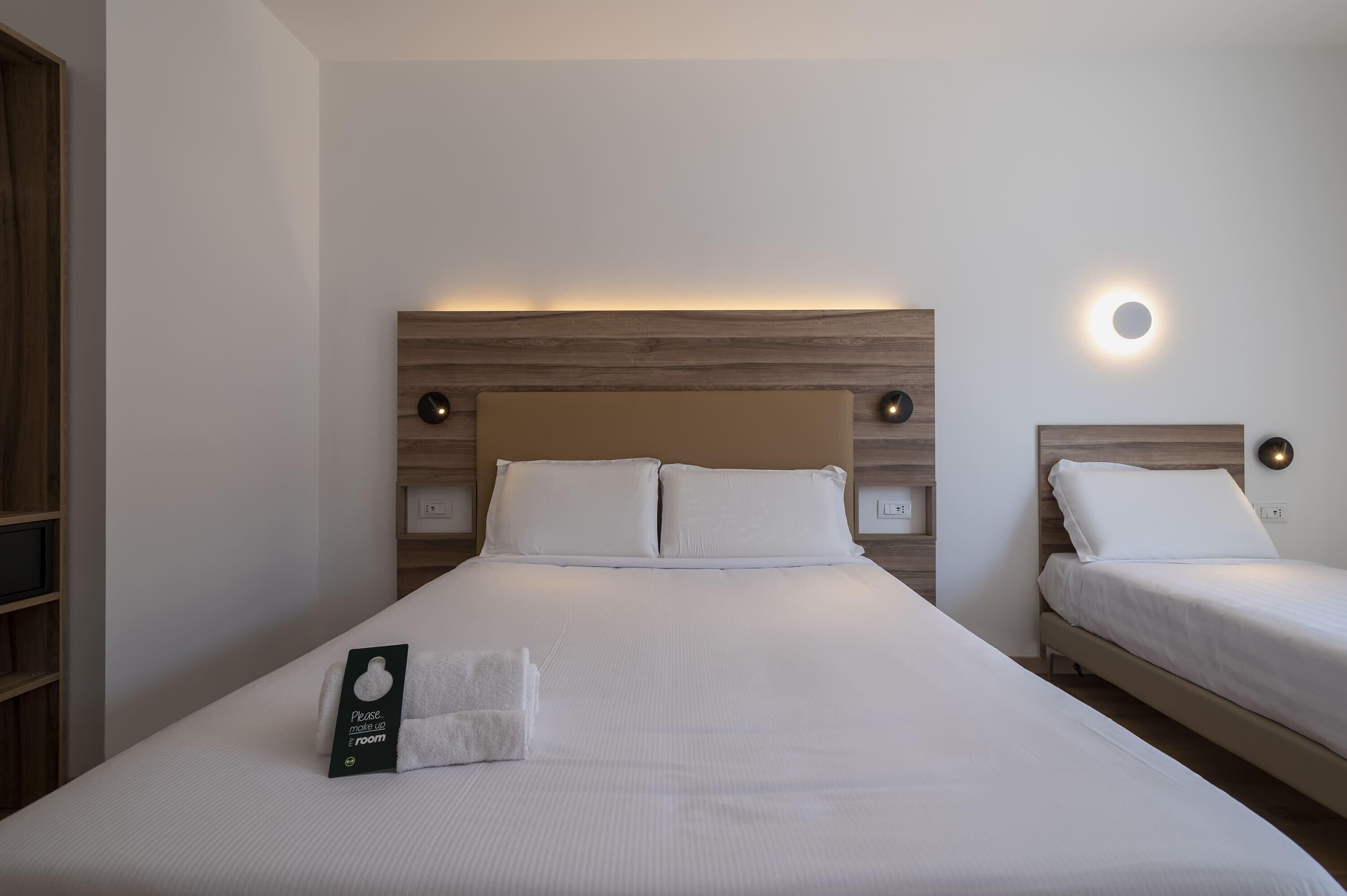 Hotellihuone, jossa on suuri sänky, kaksi yöpöytää, yövalaisin ja seinään kiinnitetty valaisin.