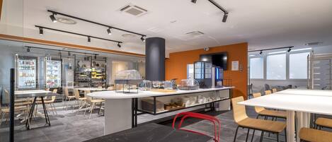 A modern dining area with a central island, seating arrangements, and a visible kitchen area with a refrigerator and shelves.