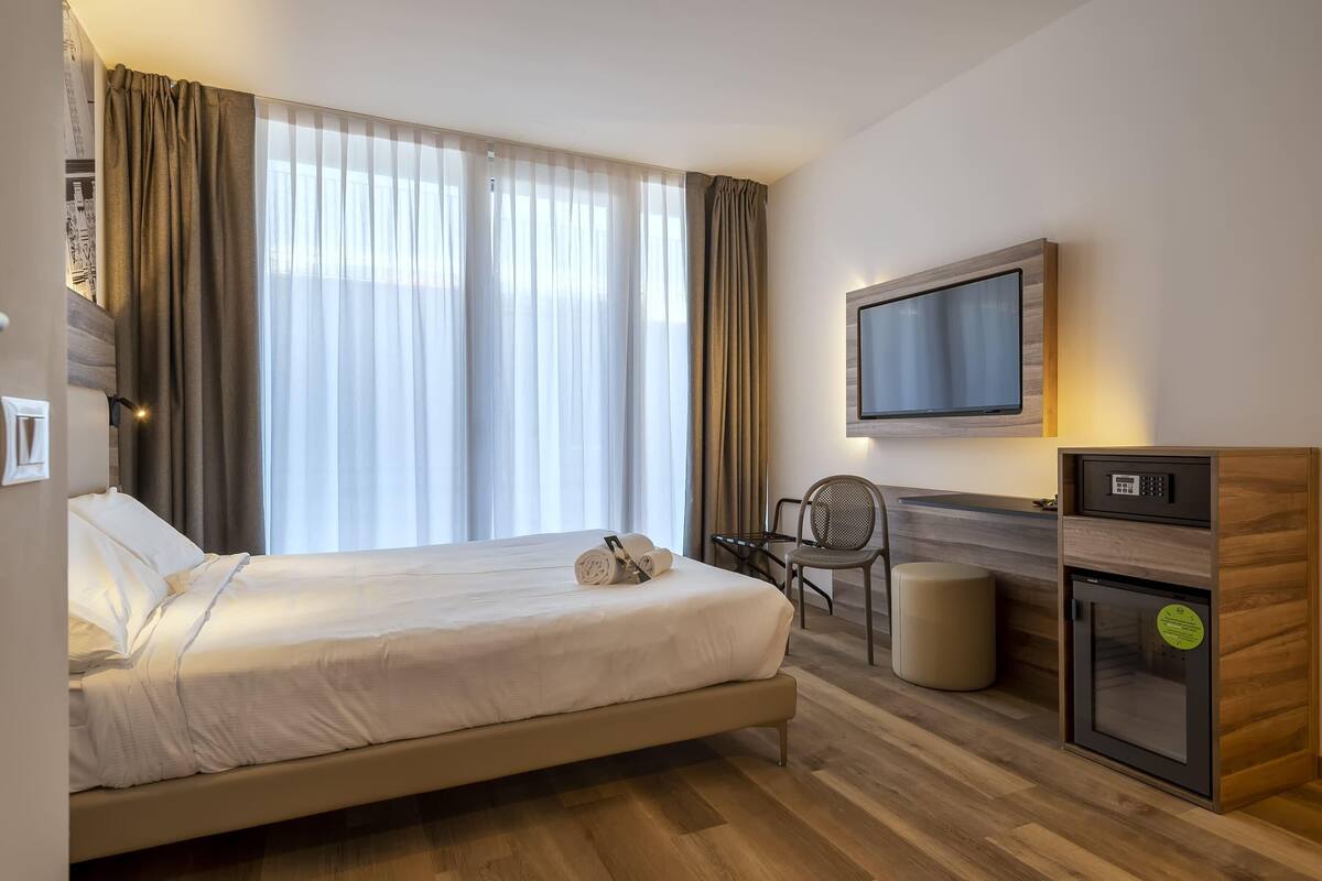 Una camera d'albergo con un letto, una scrivania, una televisione e un frigobar.