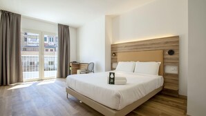 Una habitación de hotel moderna con una cama grande, suelo de madera, vistas a través de un ventanal corredero y un escritorio con una silla.