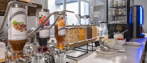 A self-serve station with various food and drink dispensers, including a hazelnut cream dispenser and a fruit punch dispenser.