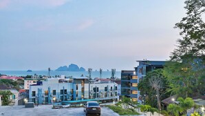 A modern building complex with multiple floors, a parking area, and a view of the sea and distant islands. - B306 - 1 Bedroom Condo Pool View Near Ao Nang Beach (Krabi)