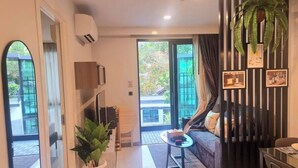 A modern living room with a sofa, a small table, and a potted plant. There is a sliding glass door leading to an outdoor area. - B306 - 1 Bedroom Condo Pool View Near Ao Nang Beach (Krabi)