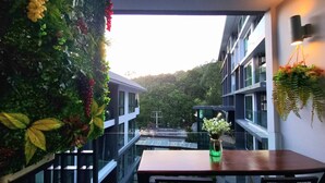 A modern building with a glass balcony, a wooden table, and a vase with flowers. - B306 - 1 Bedroom Condo Pool View Near Ao Nang Beach (Krabi)