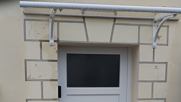 Puerta blanca con ventanal negro, incrustada en una pared de ladrillo color crema.