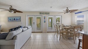 Un'ampia zona giorno con divano, tavolo da pranzo e sedie, una ventola a soffitto e un cartello con scritto "Beach House".