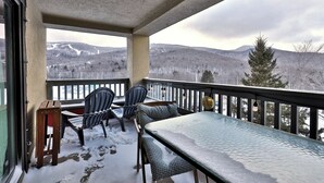 A balcony with a view of snow-covered mountains, a table, and two chairs. - Mountain Views at Mt Green: 2 BR/2BA, Shuttle, Discounted Ski Rentals, Pool, Hot Tub and More! (Killington)