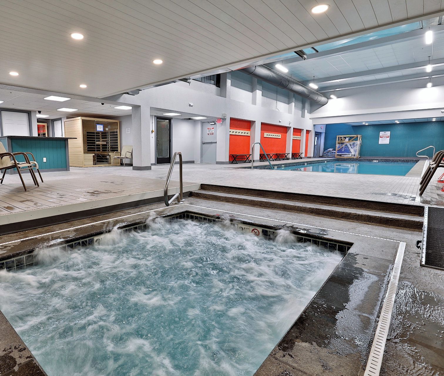 An indoor swimming pool with a hot tub, seating area, and a view of the sky through the ceiling.