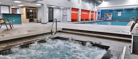 An indoor swimming pool with a hot tub, seating area, and a view of the sky through the ceiling.