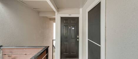 A narrow hallway with a wooden railing on one side, a dark door at the end, and a white wall with a number '2010' above it.