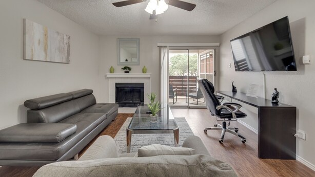 A living room with a gray sofa, a coffee table, a fireplace, a television, and a sliding glass door leading to an outdoor area.