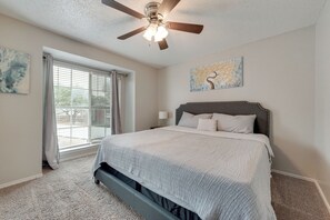 A bedroom with a bed, a ceiling fan, a window with blinds, and a painting on the wall.