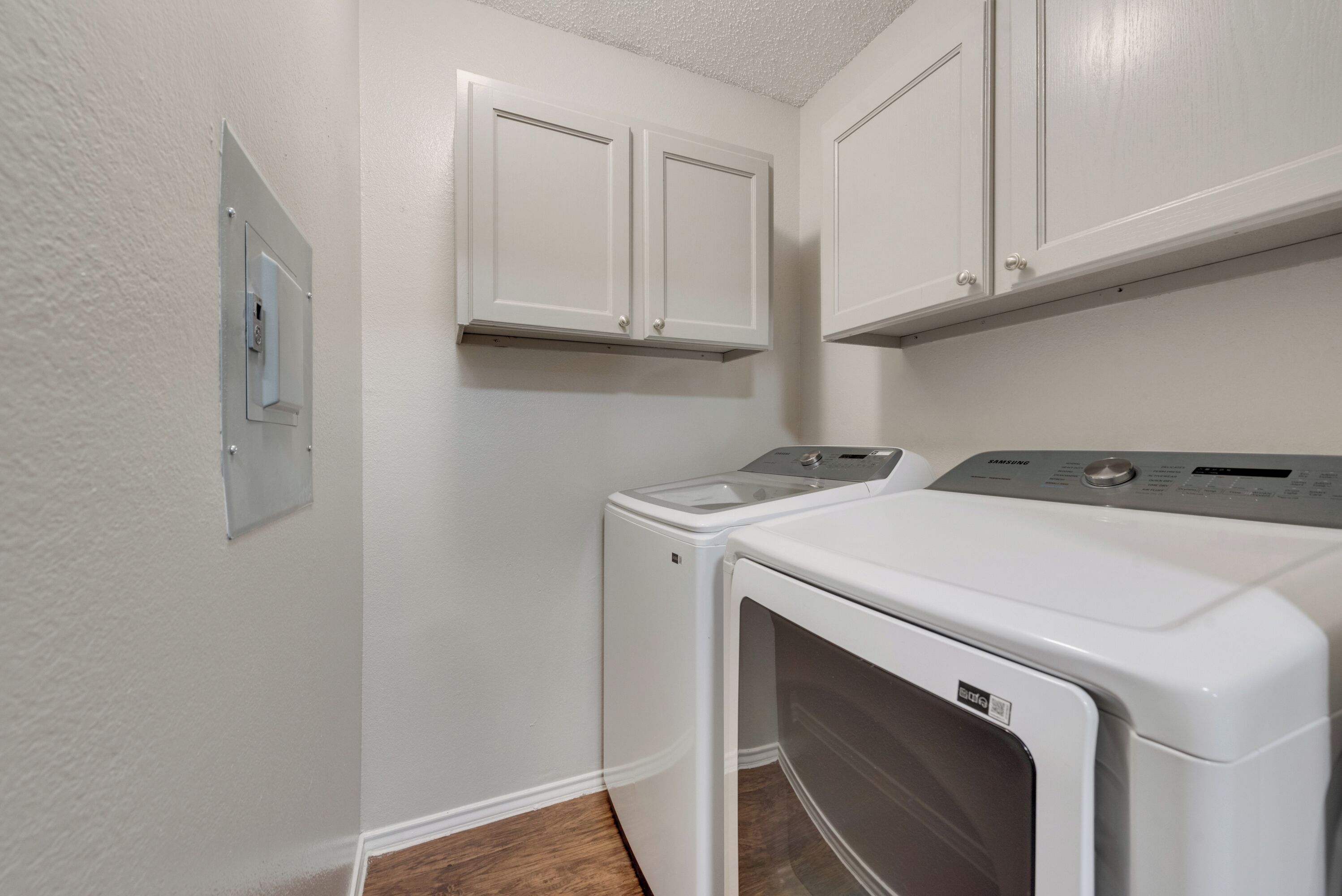 A laundry room with a front-loading washer and dryer, white cabinets above, and a thermostat on the wall.