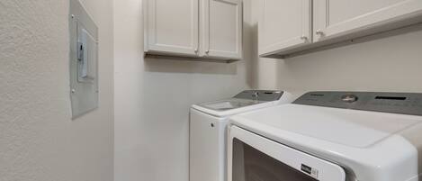 A laundry room with a front-loading washer and dryer, white cabinets above, and a thermostat on the wall.