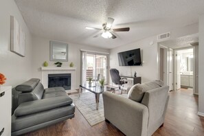 Ein modernes Wohnzimmer mit Kamin, Ledersofas, einem Glastisch und einem Deckenventilator.