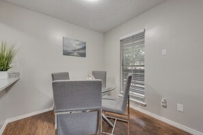 A dining area with a table and chairs, a painting on the wall, and a window with blinds.