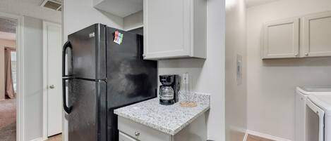 A compact kitchen with a black refrigerator, a coffee maker, and a trash bin.