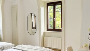 Un dormitorio con dos camas, una ventana con vistas a árboles, un escritorio con una computadora portátil y una silla.