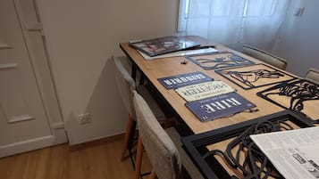 Uma área de refeições com uma mesa de madeira, cadeiras e uma janela com cortinas leves.