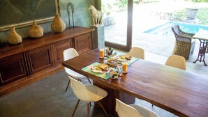 Un espace repas avec une table en bois, des chaises blanches et une vue sur une piscine.