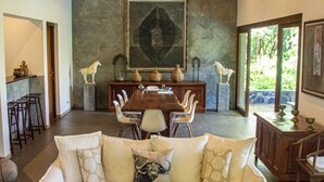 Un vaste espace de vie doté d’un plafond en bois, d’un grand tableau au mur, d’une table à manger avec des chaises et d’un canapé blanc agrémenté de coussins.
