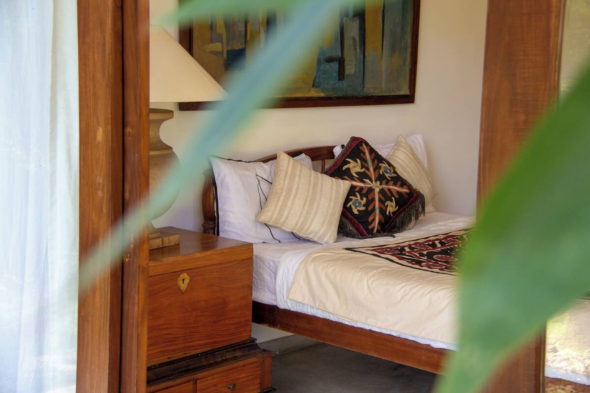 Ein hölzernes Bett mit weißer Matratze, ein Nachttisch aus Holz mit Schublade und ein Gemälde an der Wand.
