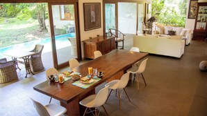 Un vaste espace dédié à la salle à manger, avec une longue table en bois, des chaises blanches et une vue sur une piscine et la verdure environnante.