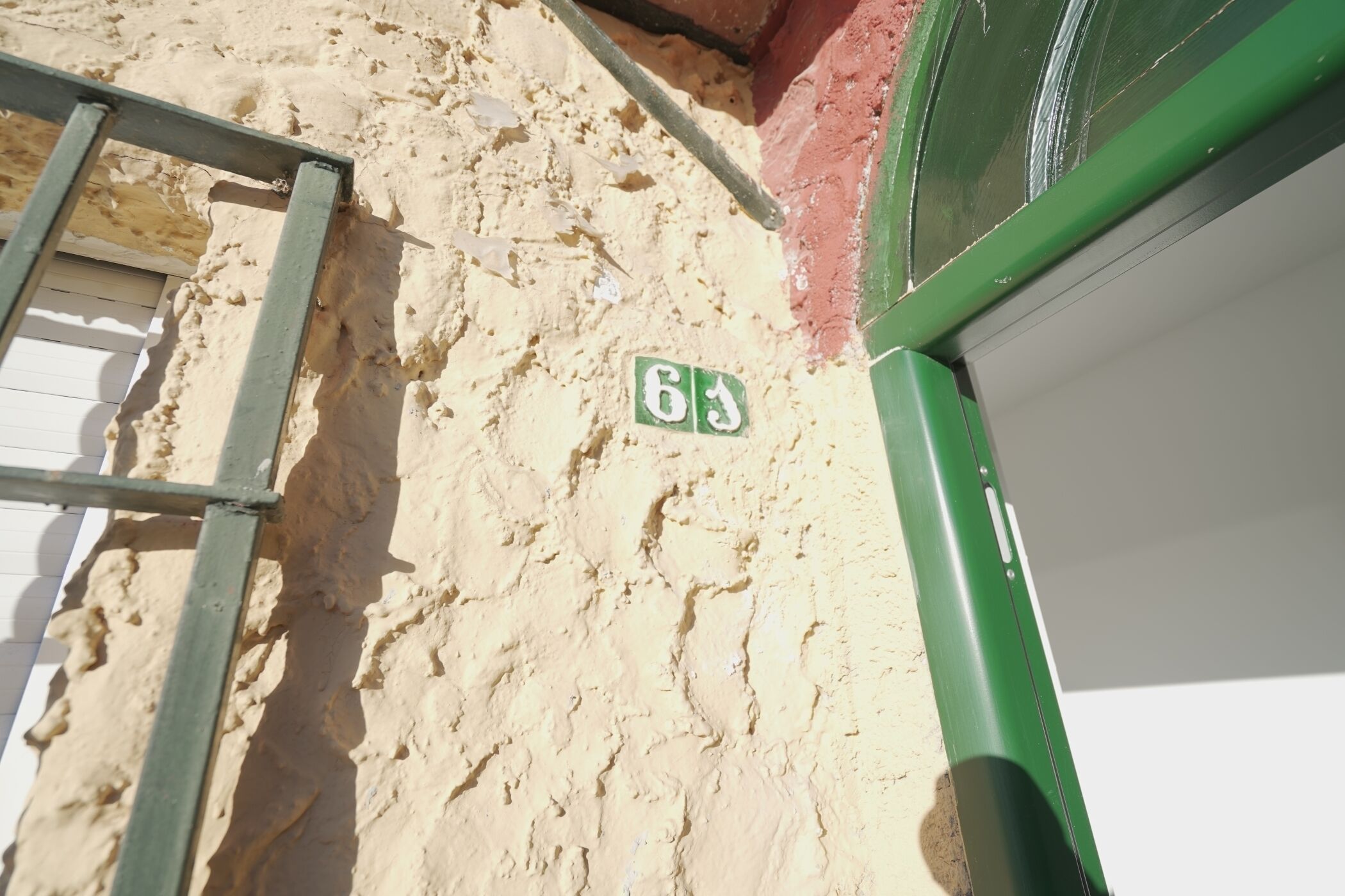 A close-up of a wall with a green metal ladder and a green door frame. A small green sign with the number "63" is visible.
