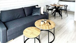 Un salon moderne avec un canapé gris, deux petites tables rondes en bois et un coin repas comprenant une table et des chaises noires.