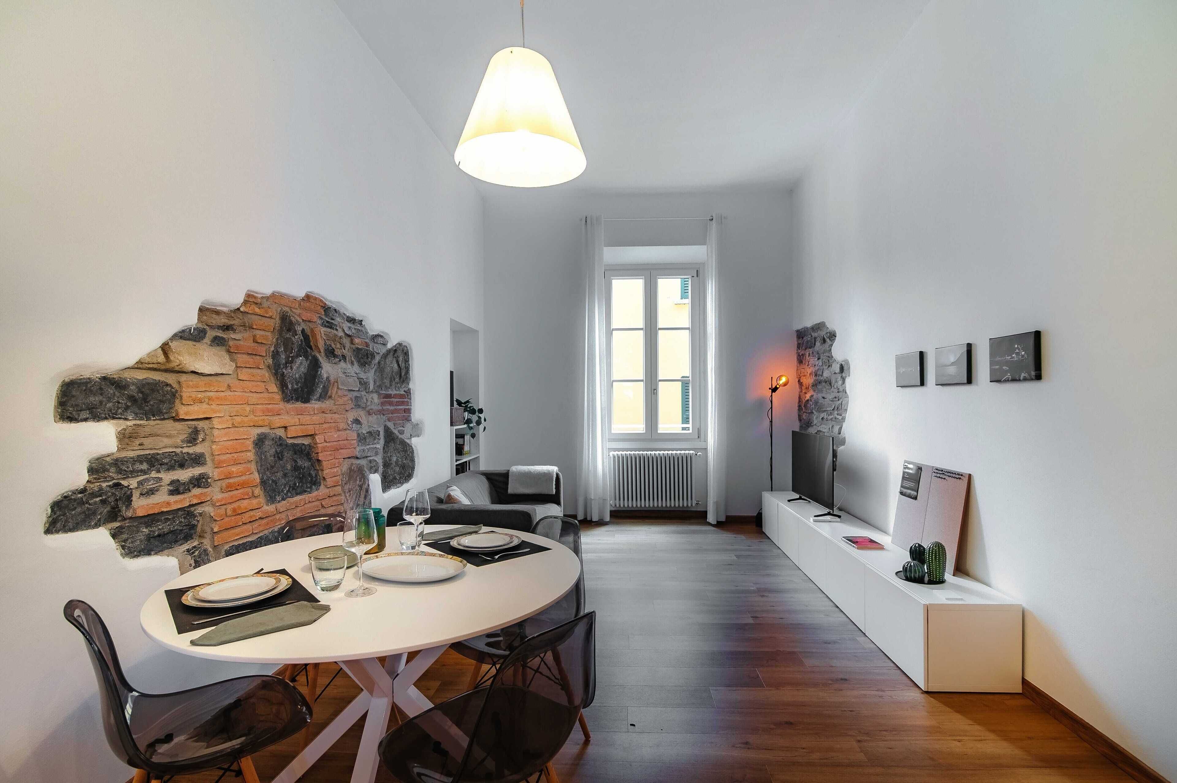 Een eethoek met een accentmuur van baksteen, een ronde tafel gedekt voor twee personen, en een moderne hanglamp.