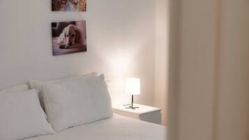 A neatly made bed with white linens, a bedside lamp, and two framed pictures of dogs on the wall.
