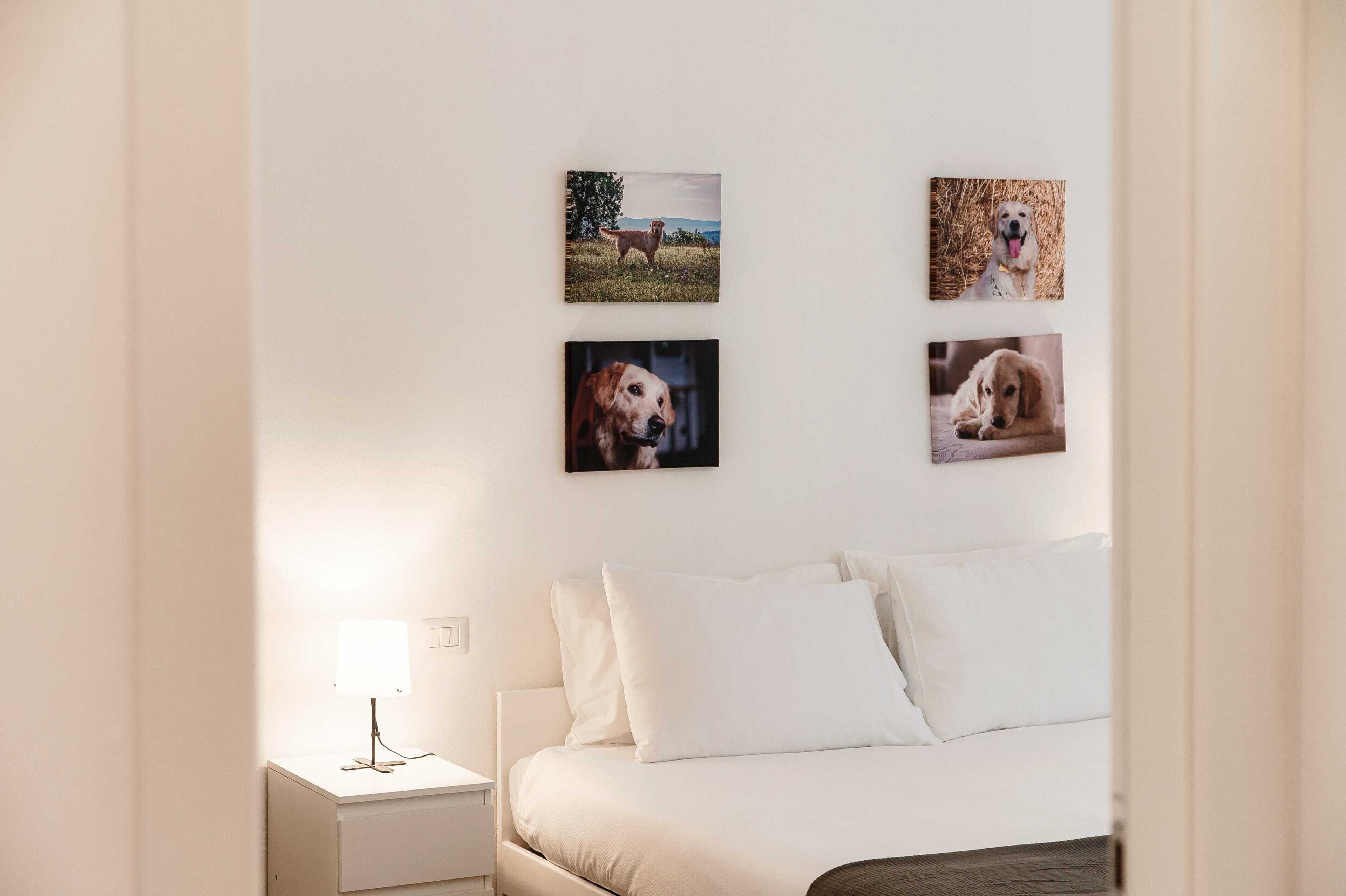 Un dormitorio con cama, mesita de noche y lámpara. Hay cuatro cuadros enmarcados en la pared.