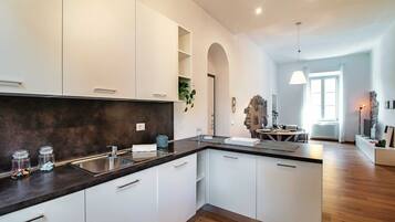A modern kitchen with white cabinets, a dark countertop, and a built-in oven. There is a dining area with a table and chairs visible through an archway.