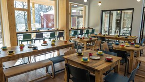 Un café spacieux avec des tables et des chaises en bois, de grandes fenêtres et une vue sur l’extérieur.
