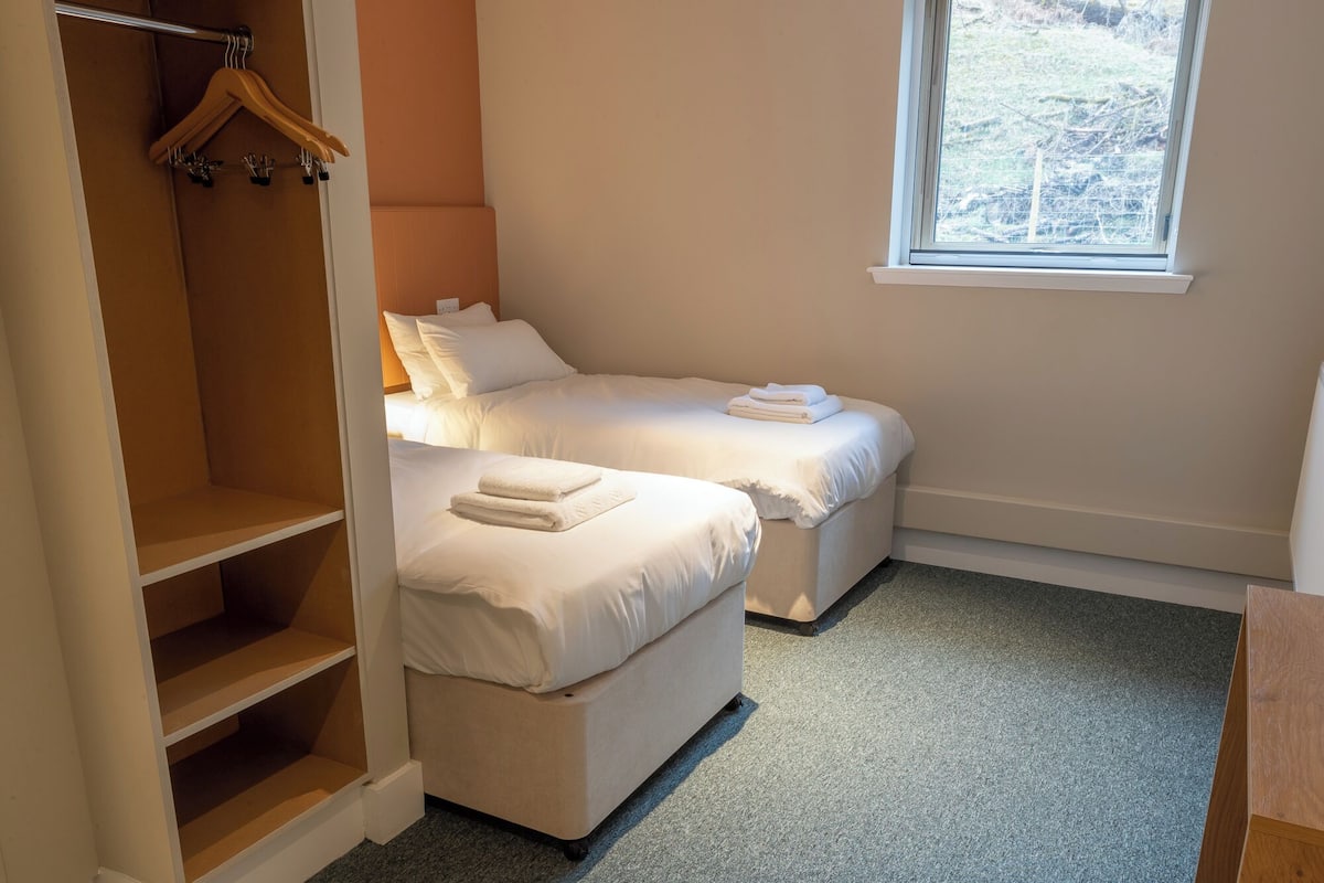 A bedroom with two beds, a wooden wardrobe, and a window.