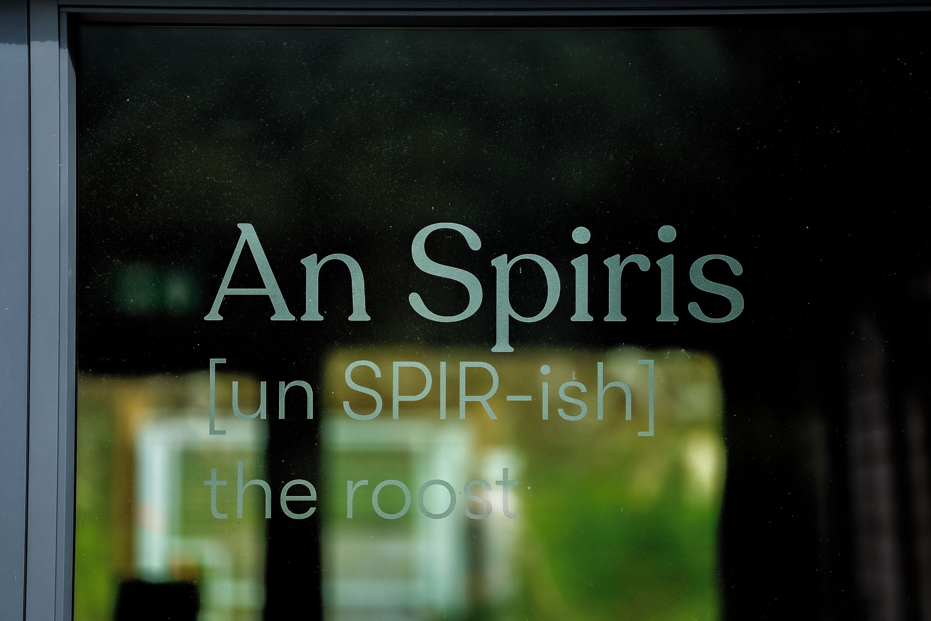 Une fenêtre sur laquelle on peut lire, à travers le verre, le texte suivant : « An Spiris [prononcé « un SPIR-ish »] the roost ».