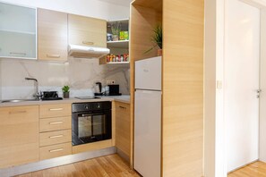 Eine kompakte Küche mit Backofen, Kühlschrank und einer Arbeitsplatte, auf der ein Wasserkocher und eine Kaffeemaschine stehen.