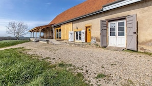 Une maison de campagne avec une allée de gravier, un porche en bois et un toit recouvert de tuiles rouges.