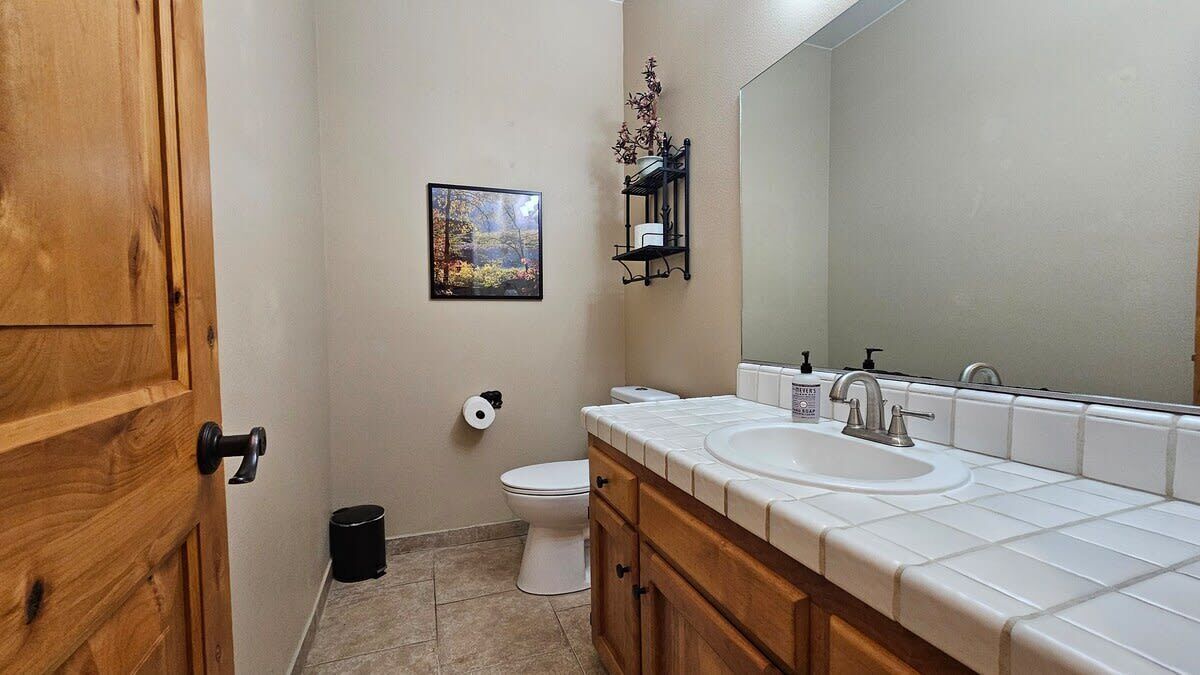 Un baño con puerta de madera, un inodoro, un lavamanos con espejo y un cuadro en la pared.
