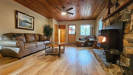 A cozy living room with a fireplace, leather sofa, wooden flooring, and a ceiling fan.