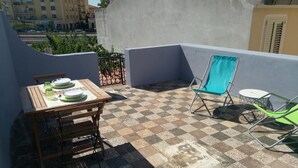 A balcony with a checkered floor, a wooden table with plates, and two chairs. - Casa Circe in Olbia With 1 Bedrooms and 1 Bathrooms (Olbia)