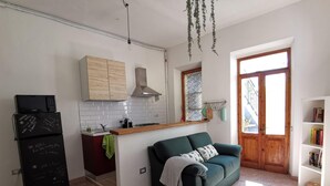 A compact living space with a kitchenette, a sofa, a bookshelf, and a door leading outside. - Casa Circe in Olbia With 1 Bedrooms and 1 Bathrooms (Olbia)